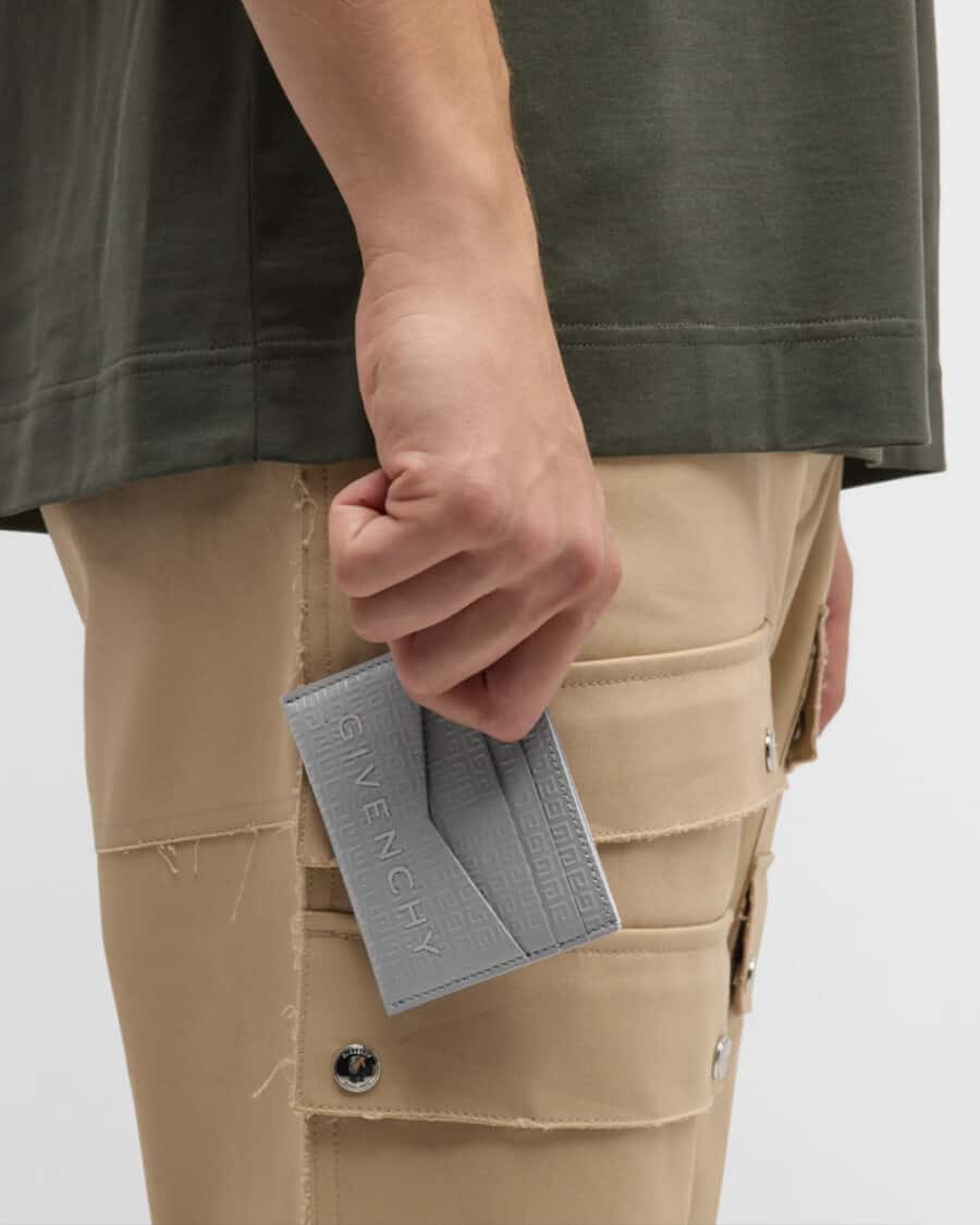 Man holding a grey leather Givenchy logo cardholder wallet wearing khaki cargo pants and green T-shirt
