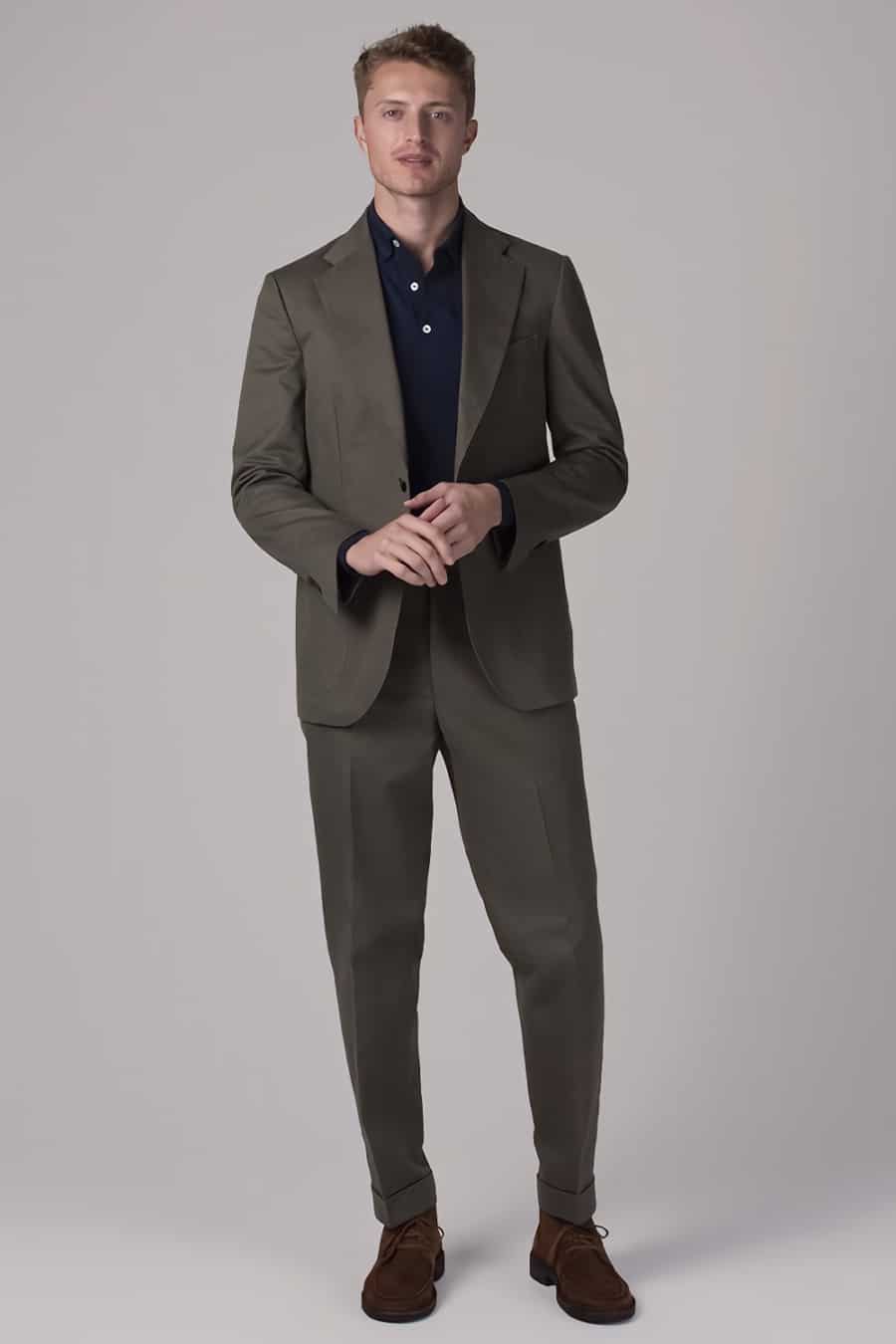 Men's olive green cotton suit, navy polo shirt and brown suede chukka boots outfit