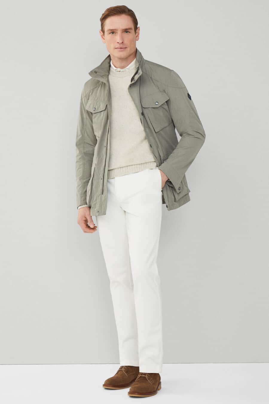 Men's white pants, white shirt, cream sweater, light green-grey field jacket and brown suede shoes smart-casual outfit