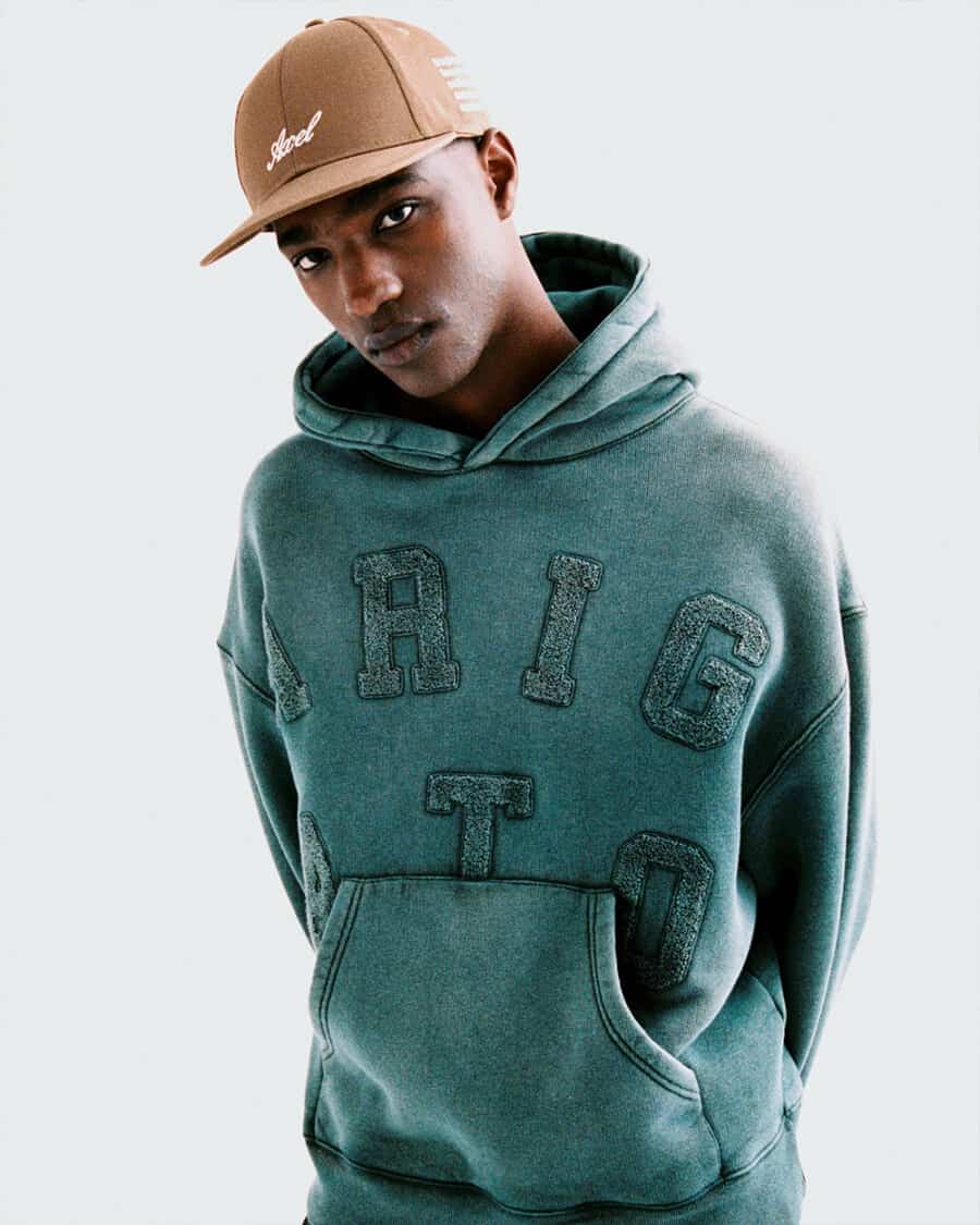Man wearing green Axel arigato streetwear hoodie and brown baseball cap