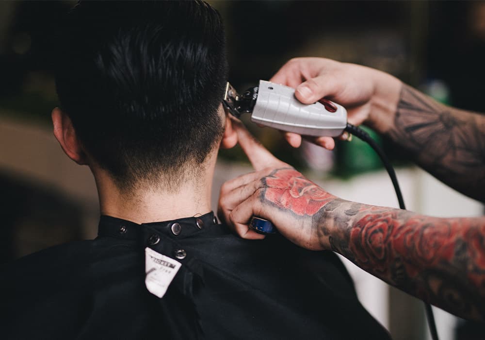 Barber giving a man a low taper fade using hair clippers