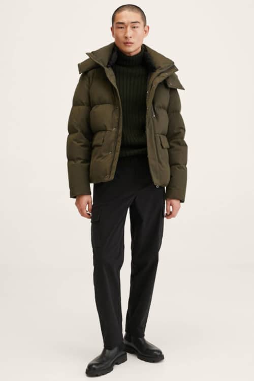 Men's black trousers, black roll neck jumper, green padded down jacket and black boots outfit