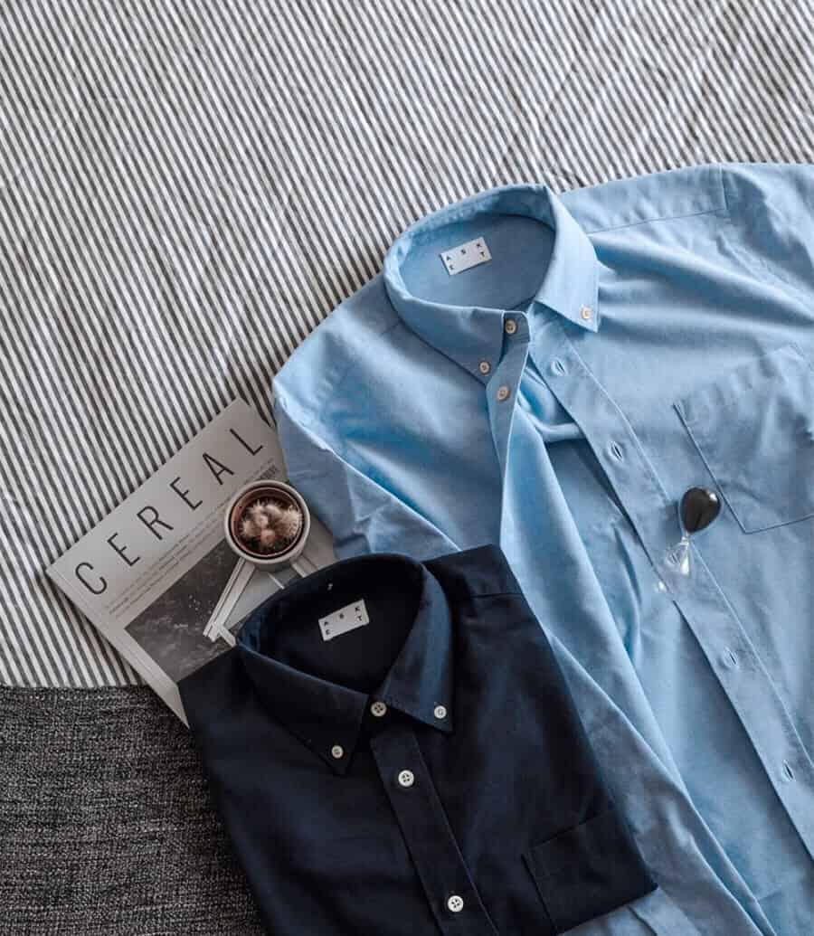 Two Oxford cloth button-down shirts in navy and sky blue laid on bed