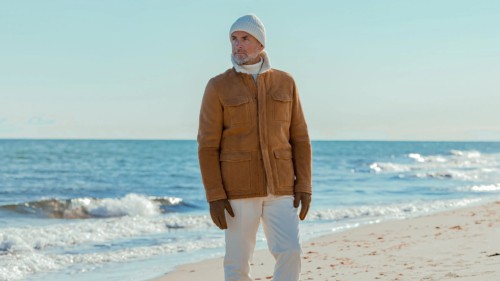 Man wearing white jeans, a beanie and a camel shearling coat