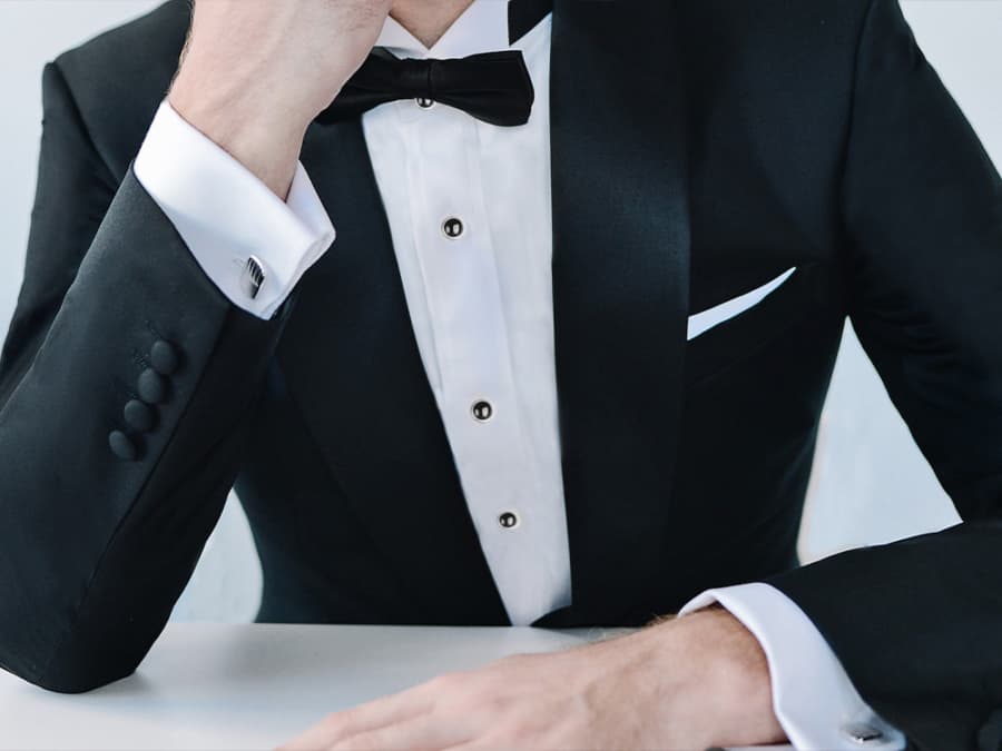 Man wearing traditional black tie accessories: silver cufflinks, black shirt studs, black bow tie and white pocket square