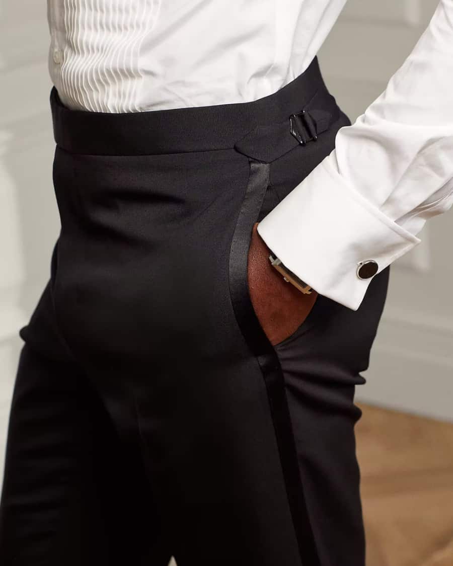 Man wearing black tie dress trousers with silk trim putting his hand in the pocket