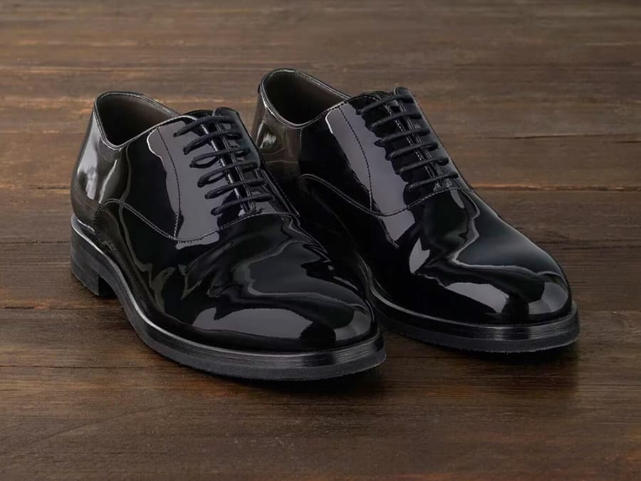 A pair of black patent leather Oxford shoes on wooden floor