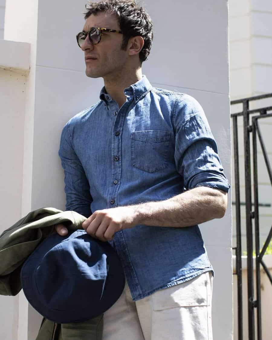 Men's mid-blue denim shirt worn with white linen trousers and sunglasses