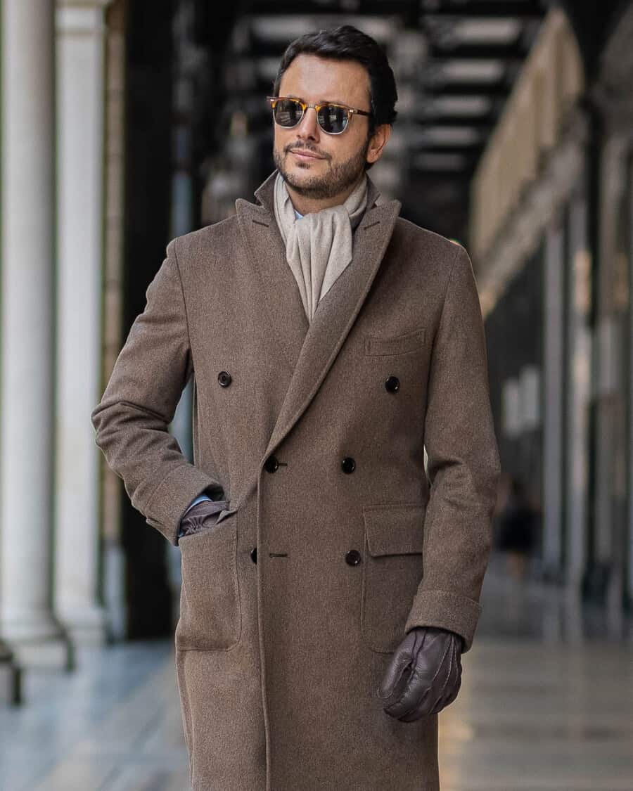 Man wearing a luxury Pini Parma made in Italy double-breasted brown overcoat with brown leather gloves and tortoiseshell sunglasses