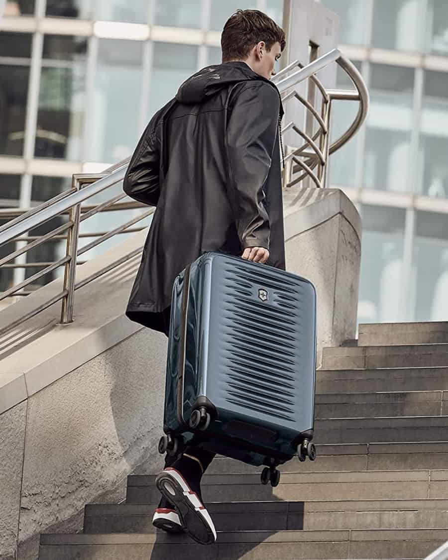 Man carrying Victorinox black wheeled suitcase up flight of stairs