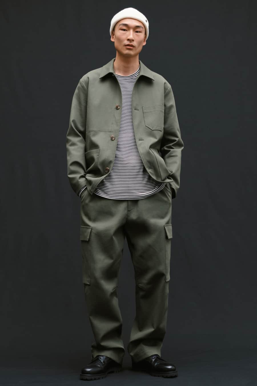 Men's matching green cargo pants and chore jacket, striped T-shirt, white beanie and black Derby shoes