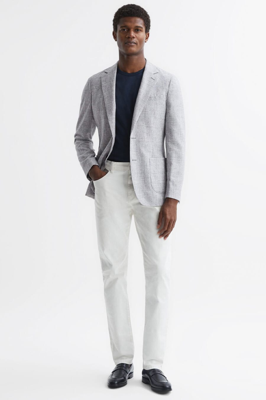 Men's white pants, tucked in navy T-shirt, light grey checked blazer and black leather penny loafers business casual outfit