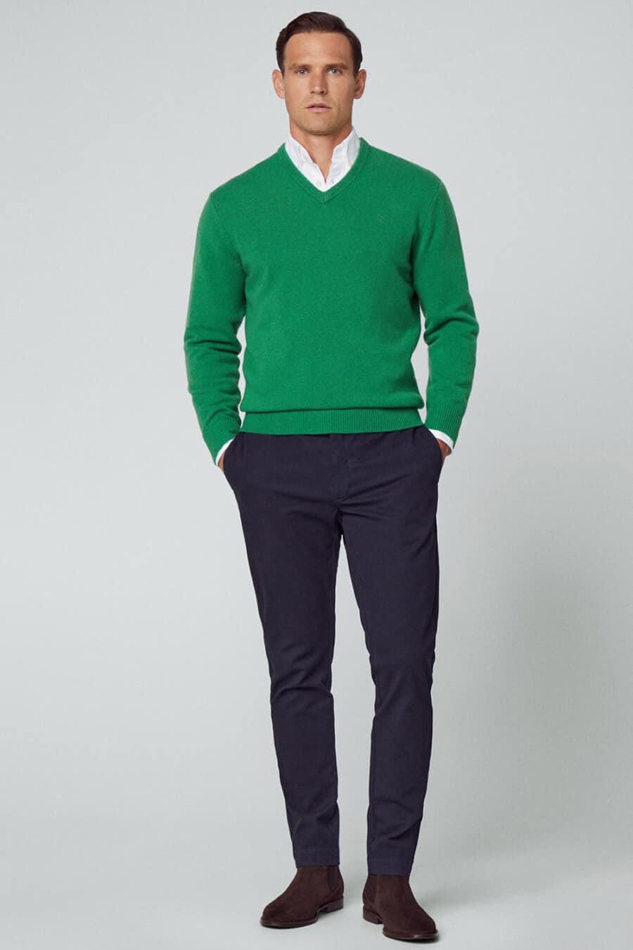 Men's navy pants, white Oxford shirt, bright green V-neck sweater and brown suede Chelsea boots business casual outfit
