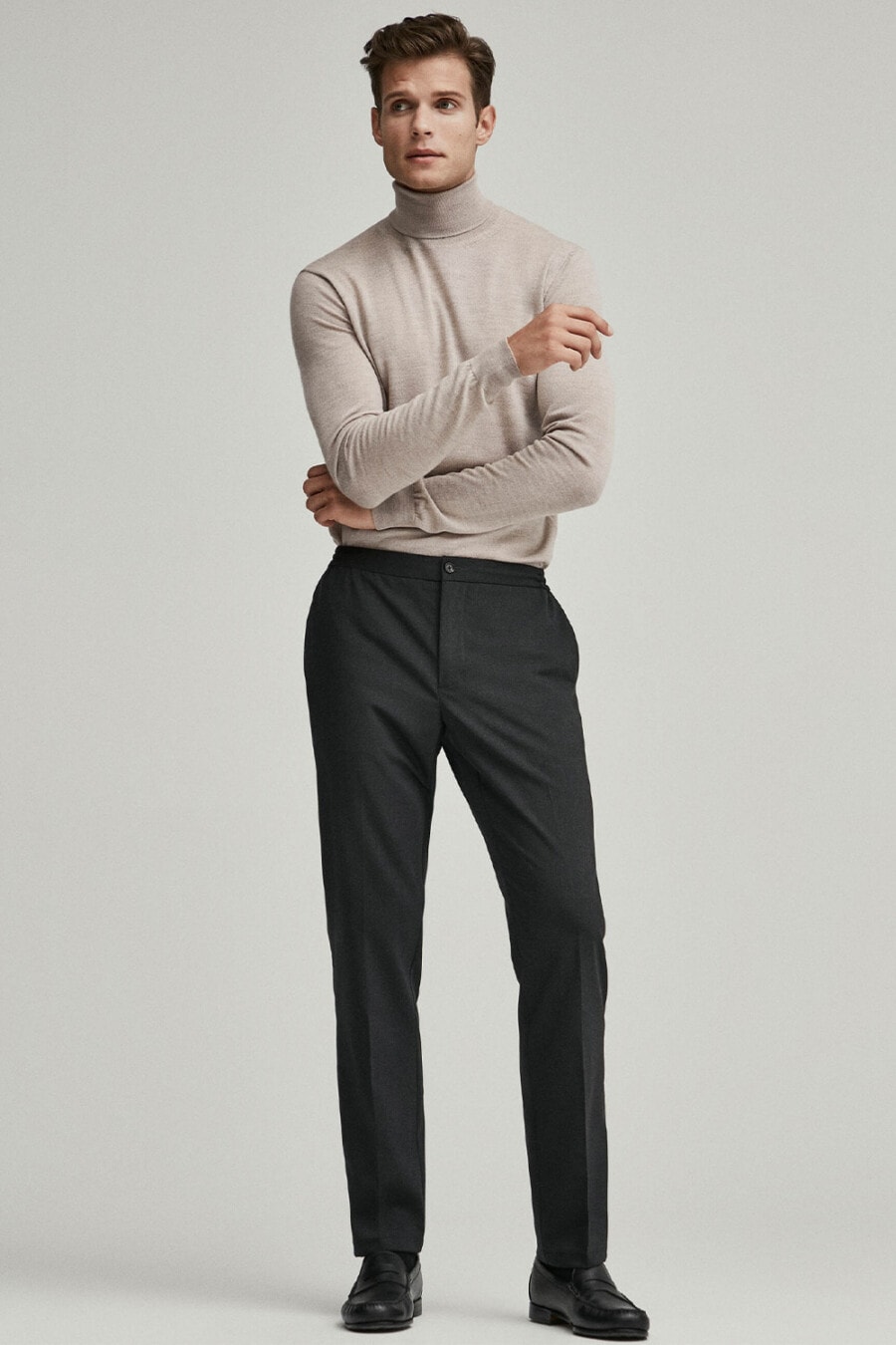 Men's charcoal tailored pants, stone tucked in turtleneck, black socks and black leather penny loafers business casual outfit