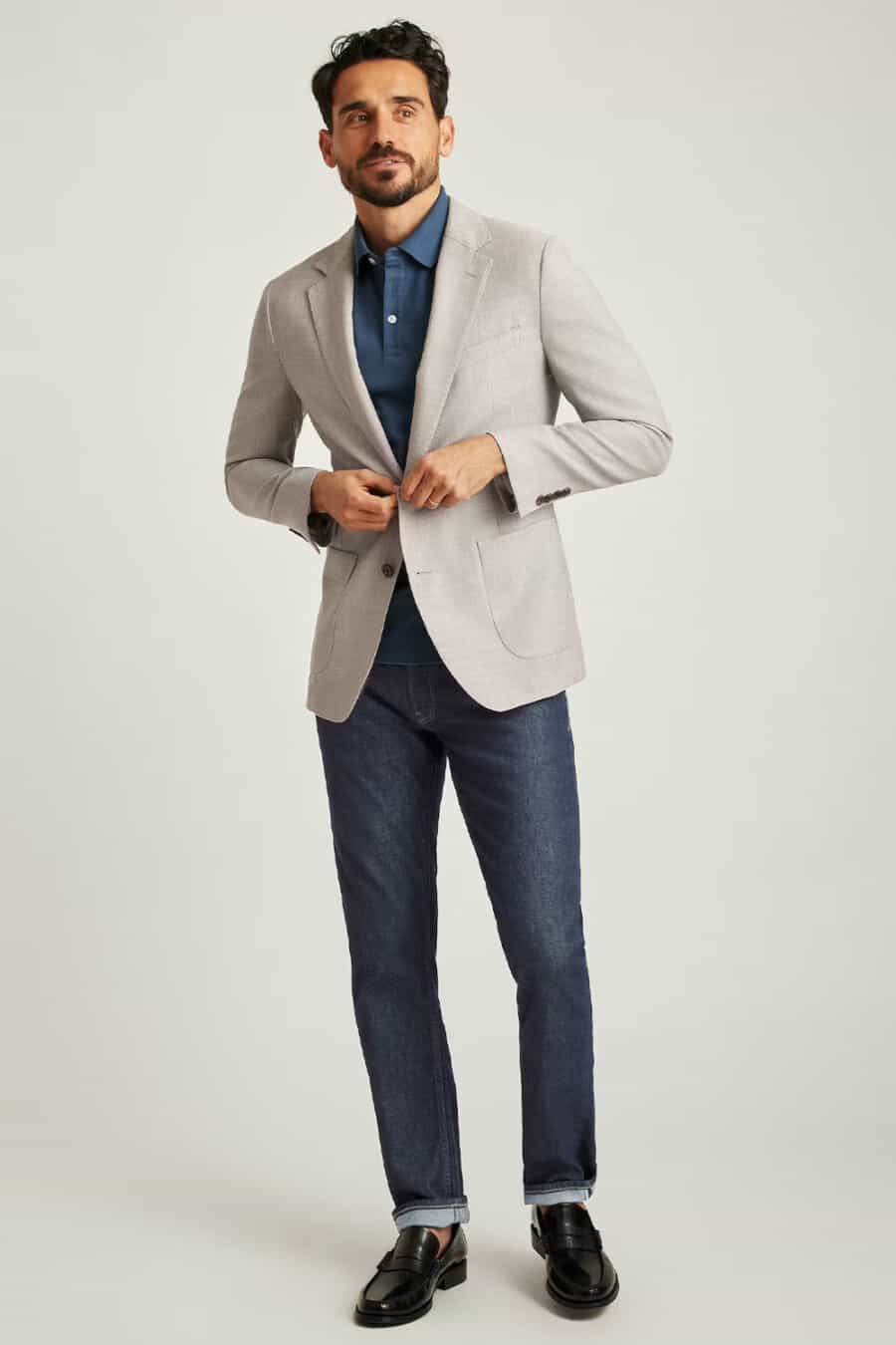 Men's raw denim jeans, mid blue polo shirt, stone blazer and black leather penny loafers business casual outfit