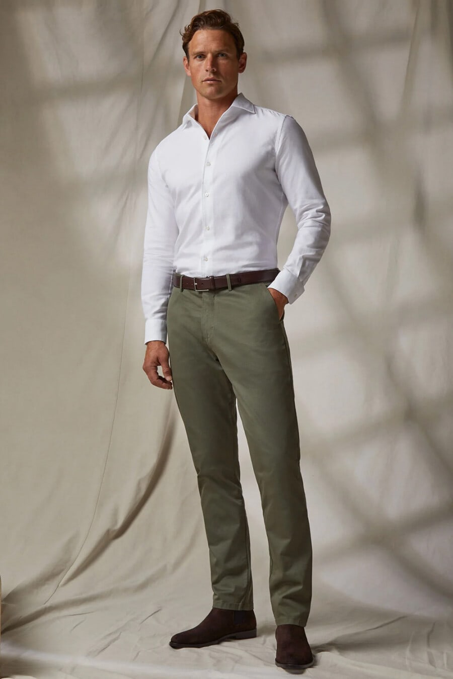 Men's green pants, white tucked in shirt, brown leather belt and brown suede Chelsea boots business casual outfit