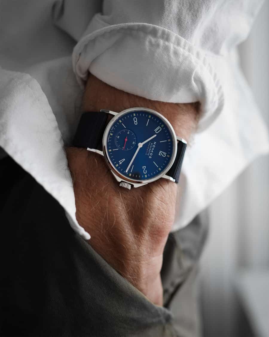 Men's NOMOS watch on wrist worn with white shirt and black trousers