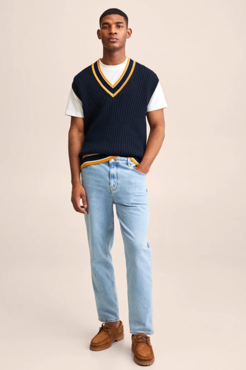 Men's light wash jeans, white T-shirt, navy sweater vest and suede deck shoes outfit