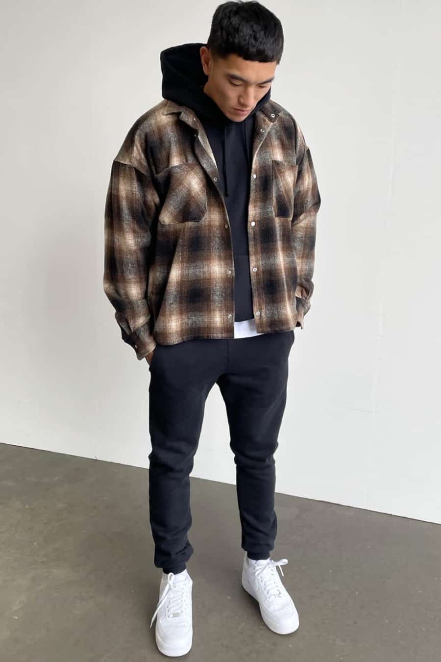 Men's black joggers, black hoodie, brown check flannel shirt and white sneakers outfit