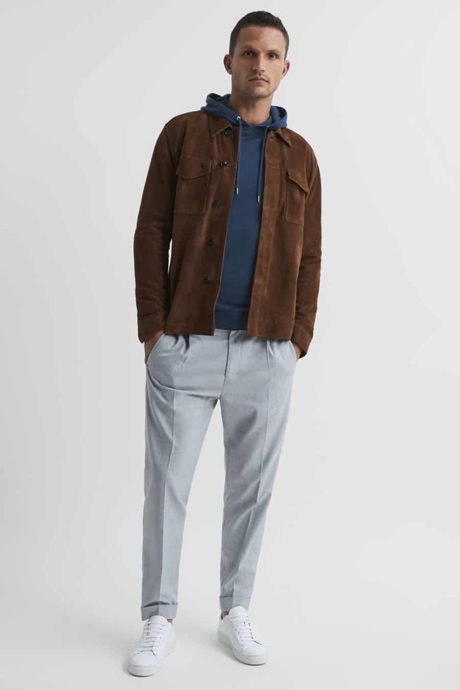 Men's grey pleated trousers, blue hoodie, brown suede jacket and white sneakers outfit