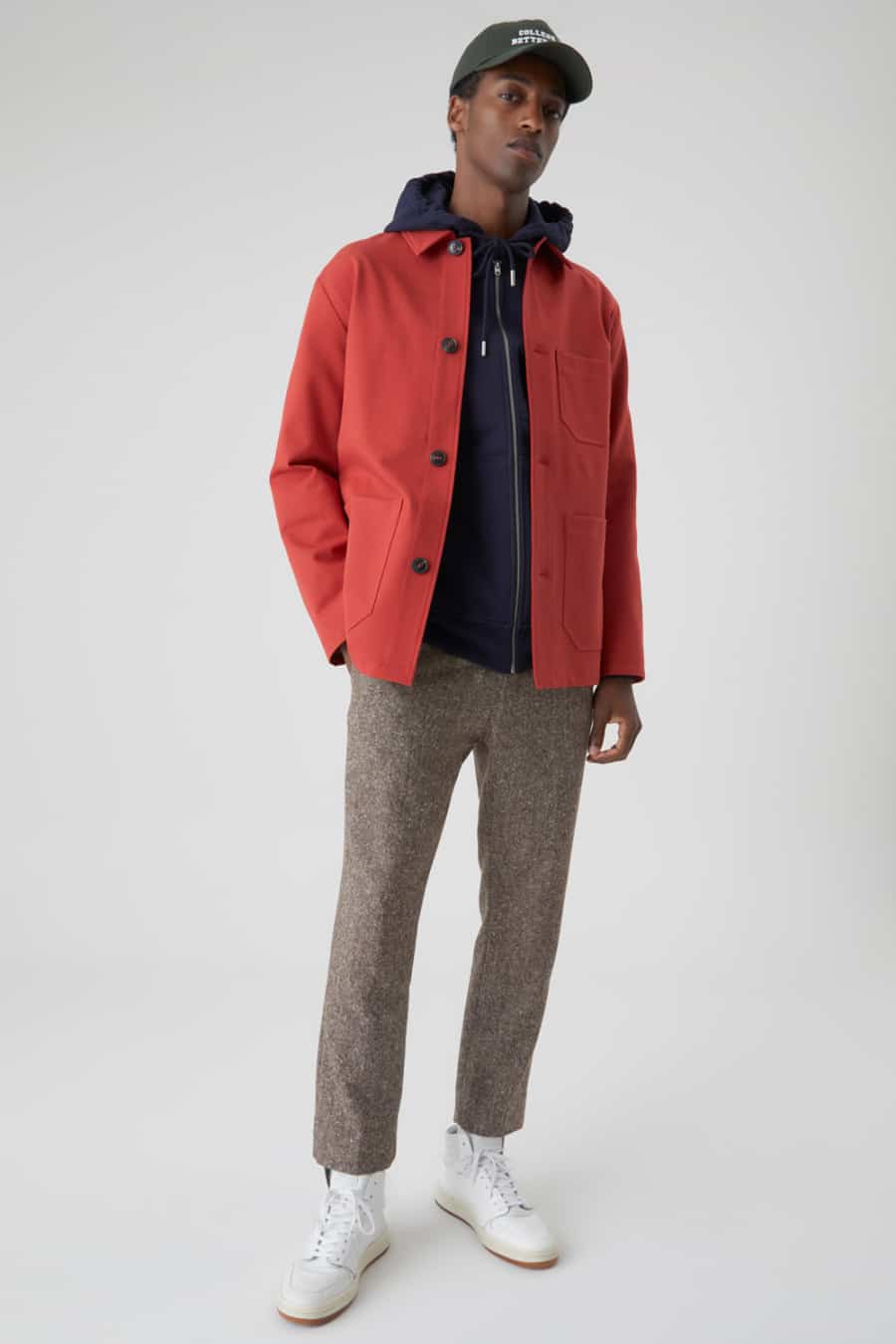Men's brown wool trousers, navy hoodie, red chore jacket and white high-top sneakers outfit