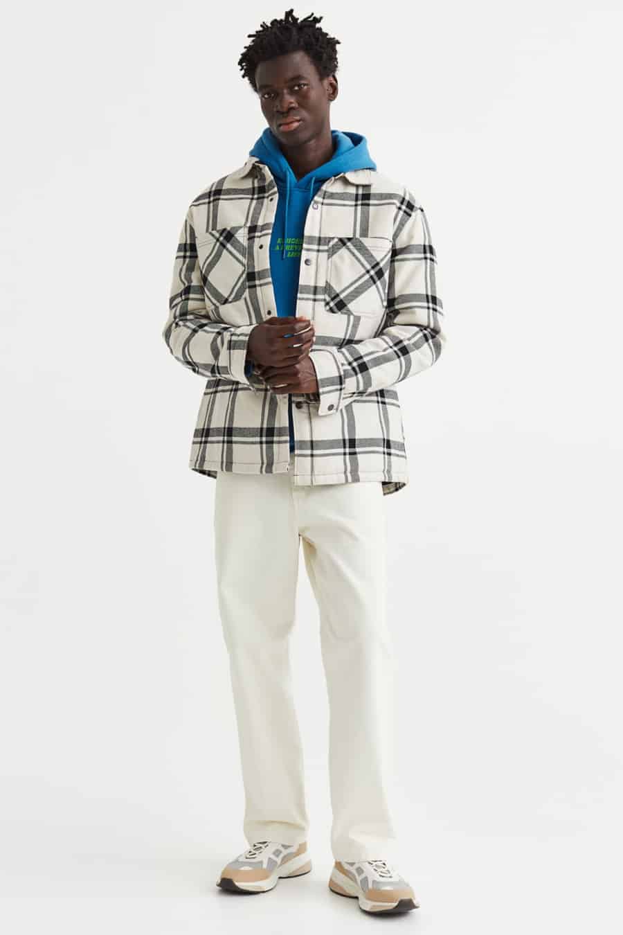 Men's white pants, bold blue hoodie, white and black checked flannel overshirt and white sneakers outfit