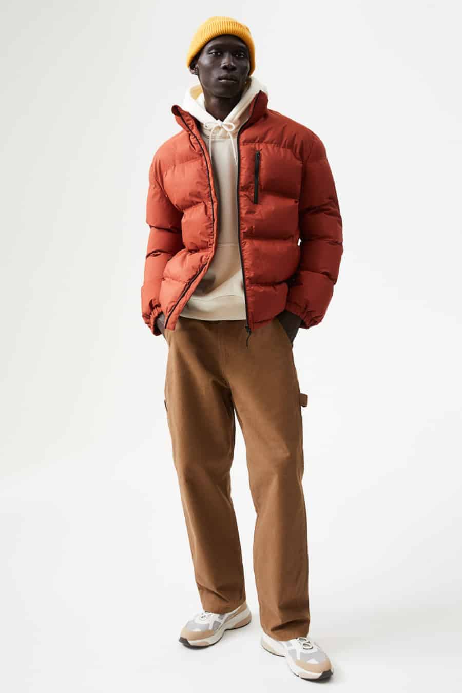 Men's brown carpenter pants, white hoodie, red puffer jacket, yellow beanie and sneakers outfit