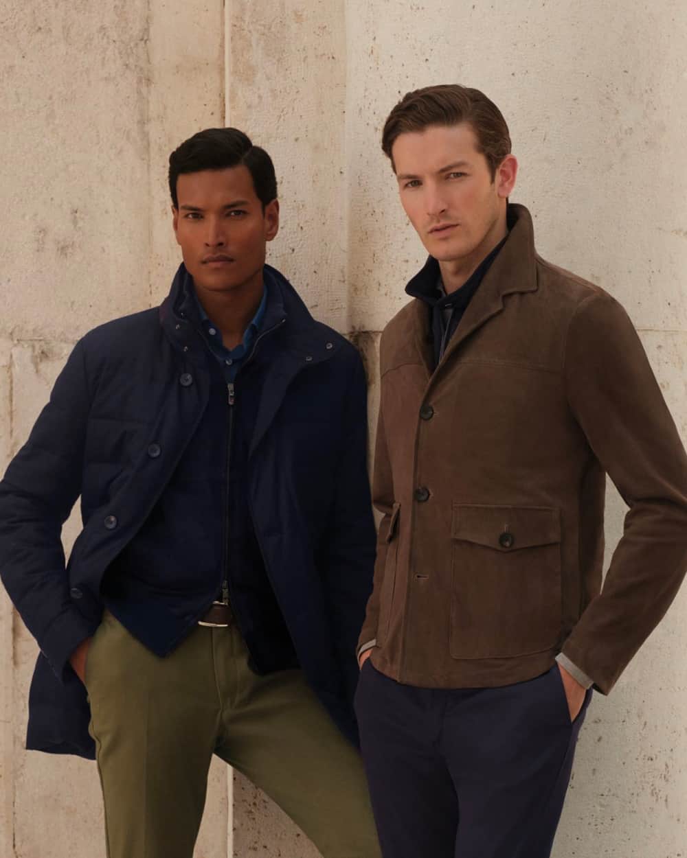 Two men wearing Hackett clothing - one in green pants, blue shirt, navy zip cardigan and a navy jacket, and the other in navy pants, navy zip up cardigan and brown suede field jacket