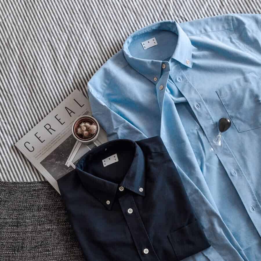 Two Oxford button-down shirts lay on a bed