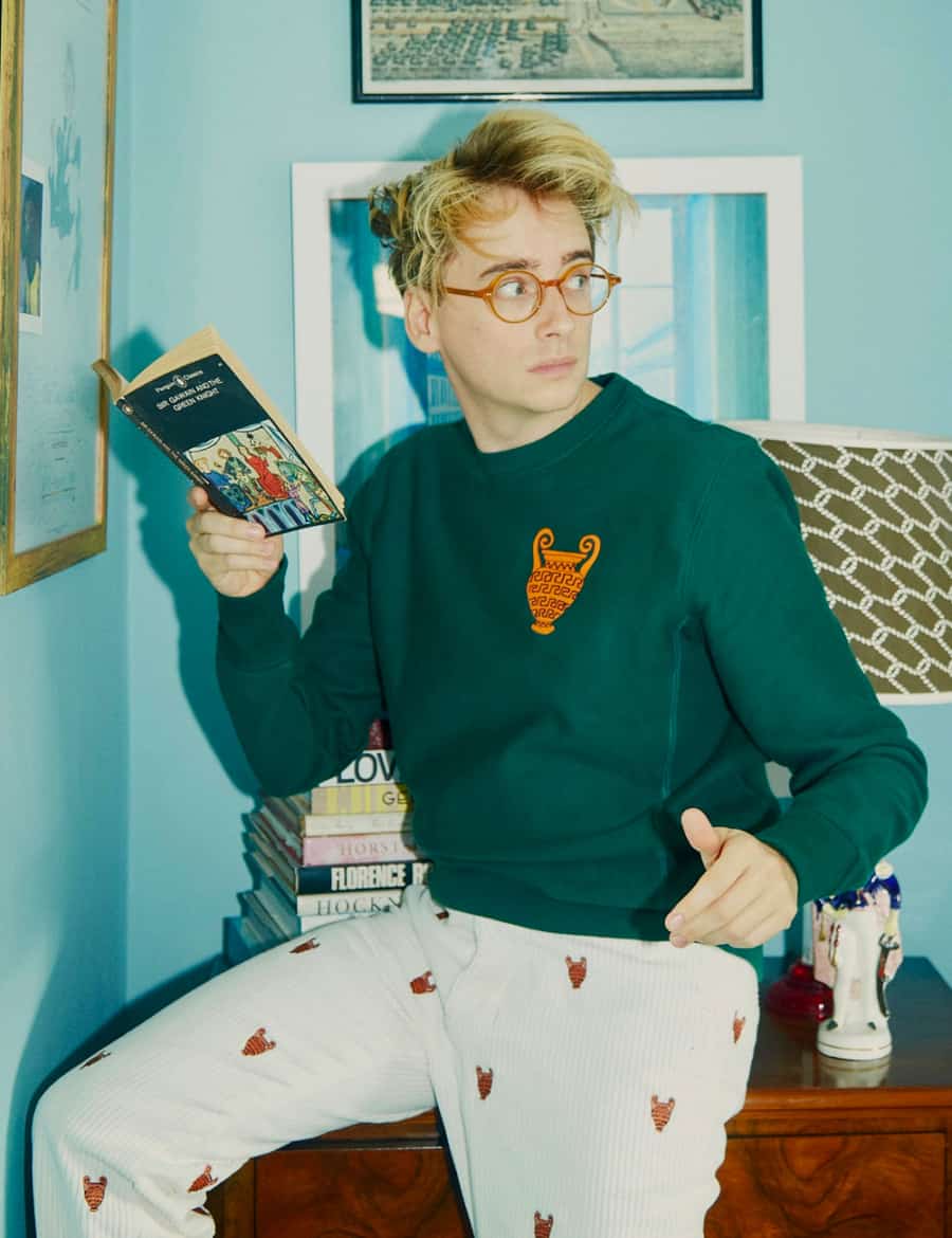 Man reading a book wearing a preppy sweatshirt and patterned trousers