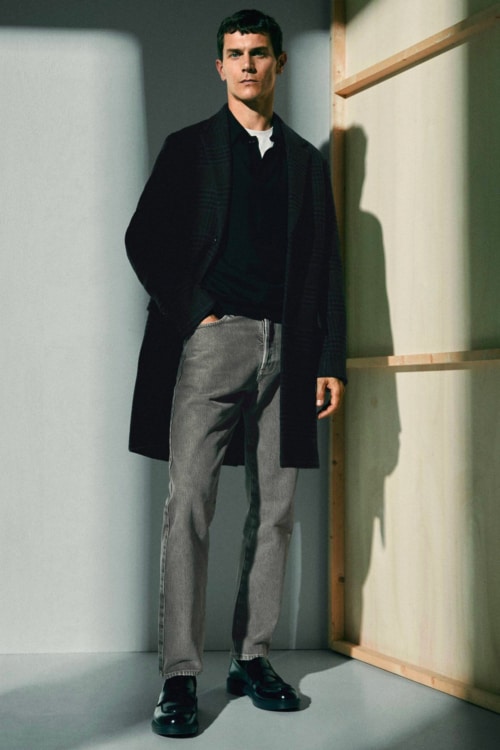 Men's grey jeans, black knitted polo shirt, black overcoat and black penny loafers outfit