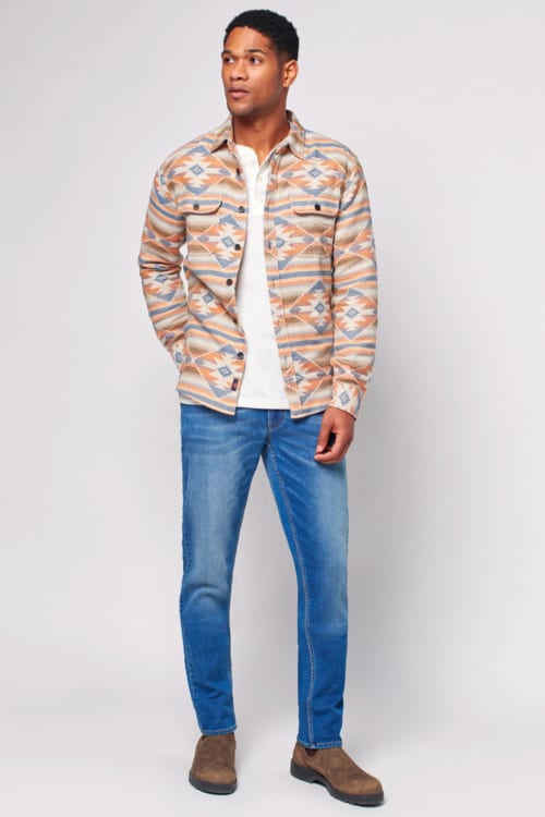 Men's mid wash jeans, white henley top, patterned overshirt and brown suede Chelsea boots outfit