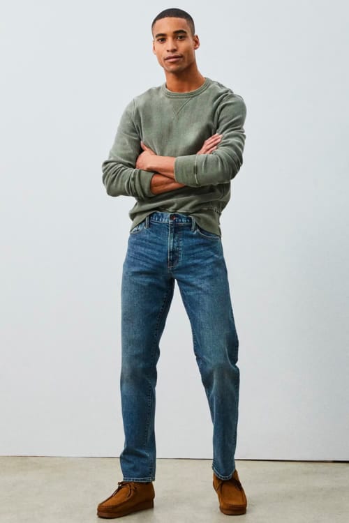 Men's mid wash jeans, green sweatshirt and tan suede wallabee shoes outfit