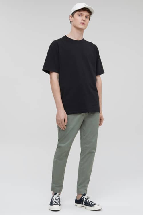 Men's green chinos, black T-shirt, white baseball cap and black canvas sneakers outfit