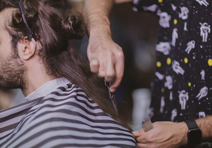 Man with long hair sat in chair getting it thinned out by barber