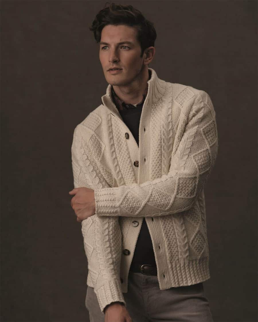 Man wearing white funnel collar cardigan over a shirt and sweater with grey jeans