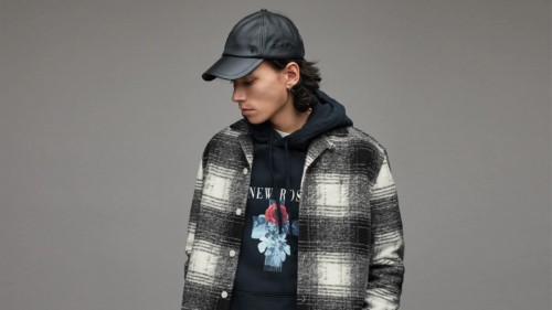 Man wearing black printed hoodie underneath a black and white checked flannel overshirt with black baseball cap