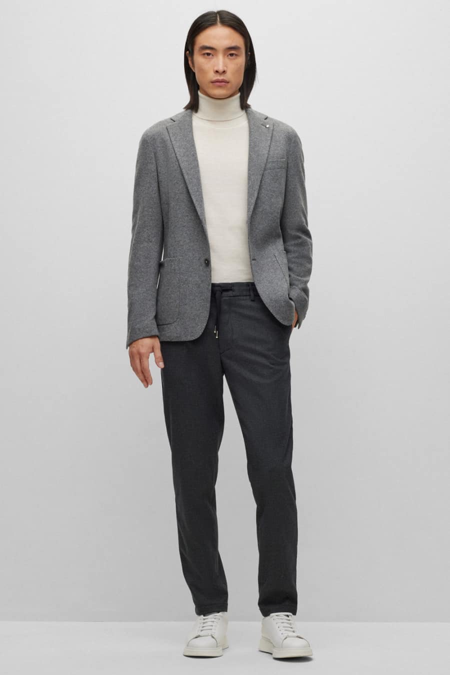Men's charcoal trousers, white roll neck, light grey blazer and white sneakers outfit
