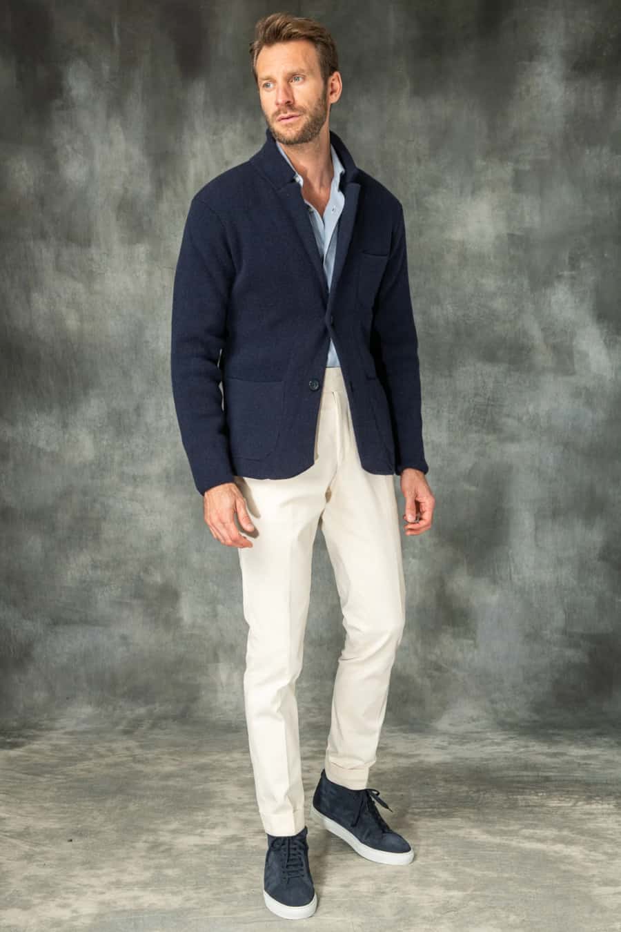 Men's white trousers, blue Oxford shirt, navy knitted blazer and navy sneakers outfit