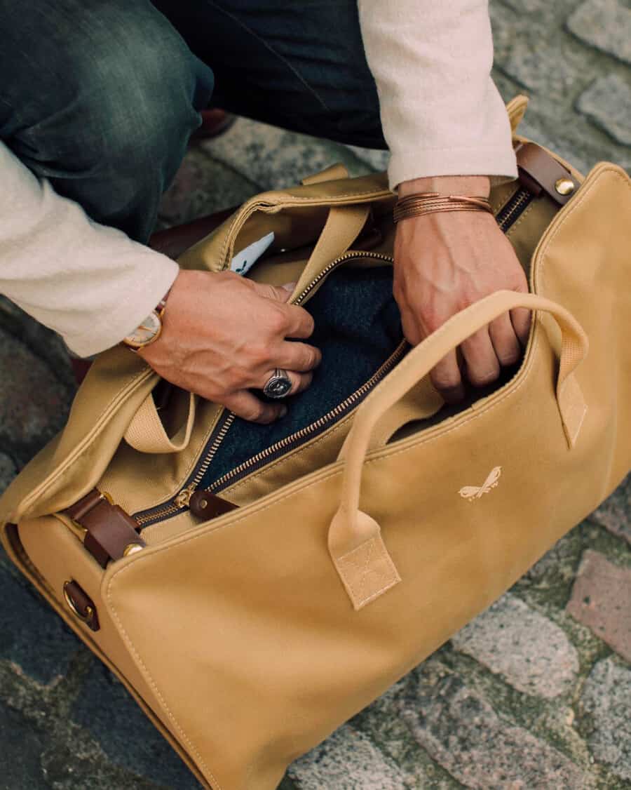 Man opening his beige canvas weekender bag to search for something inside