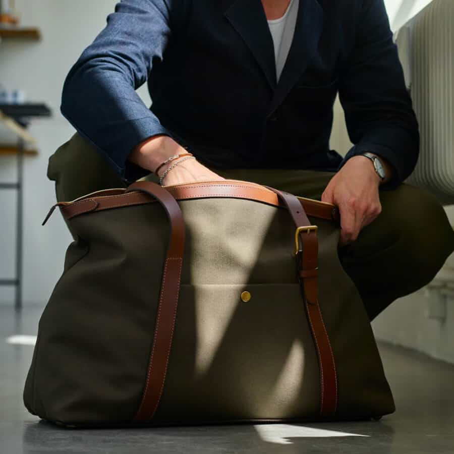 Man searching for something in his green canvas Mismo weekender bag