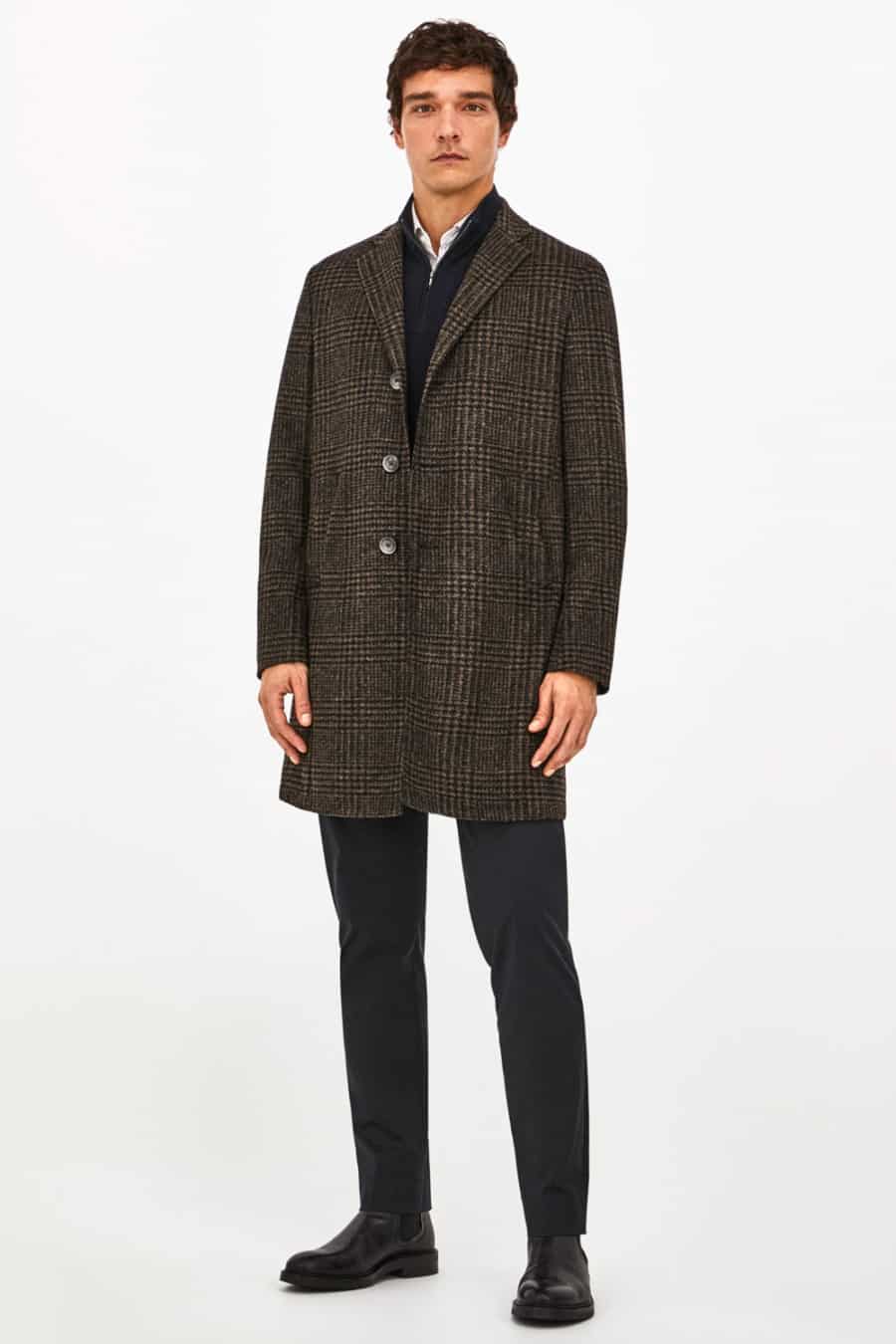 Men's black trousers, black Chelsea boots, white shirt, black zip neck sweater and brown checked overcoat outfit