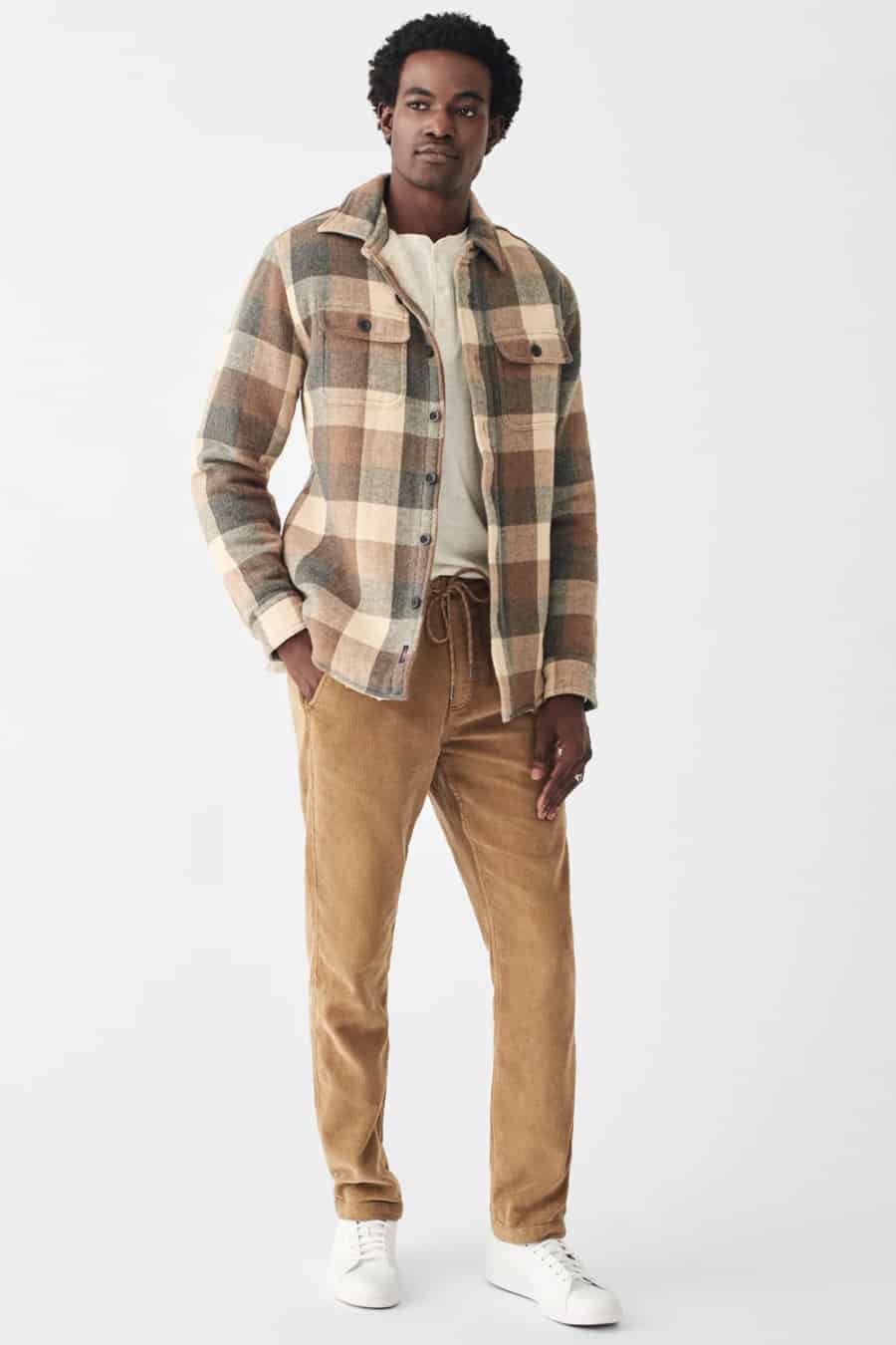 Men's corduroy trousers, white Henley shirt, checked flannel overshirt and white sneakers outfit