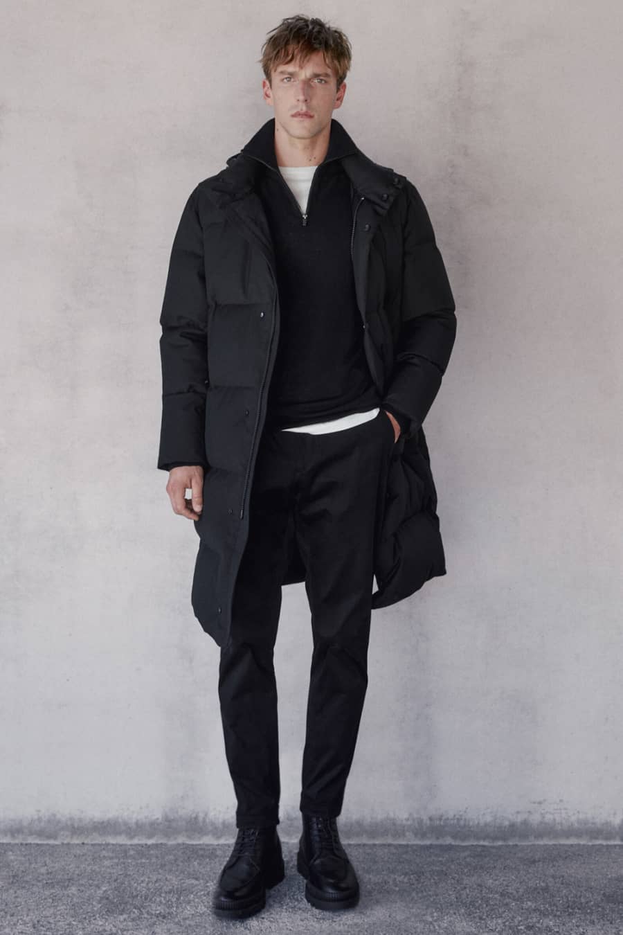 Men's black jeans, white T-shirt, black funnel neck sweater, black puffer jacket and black boots outfit