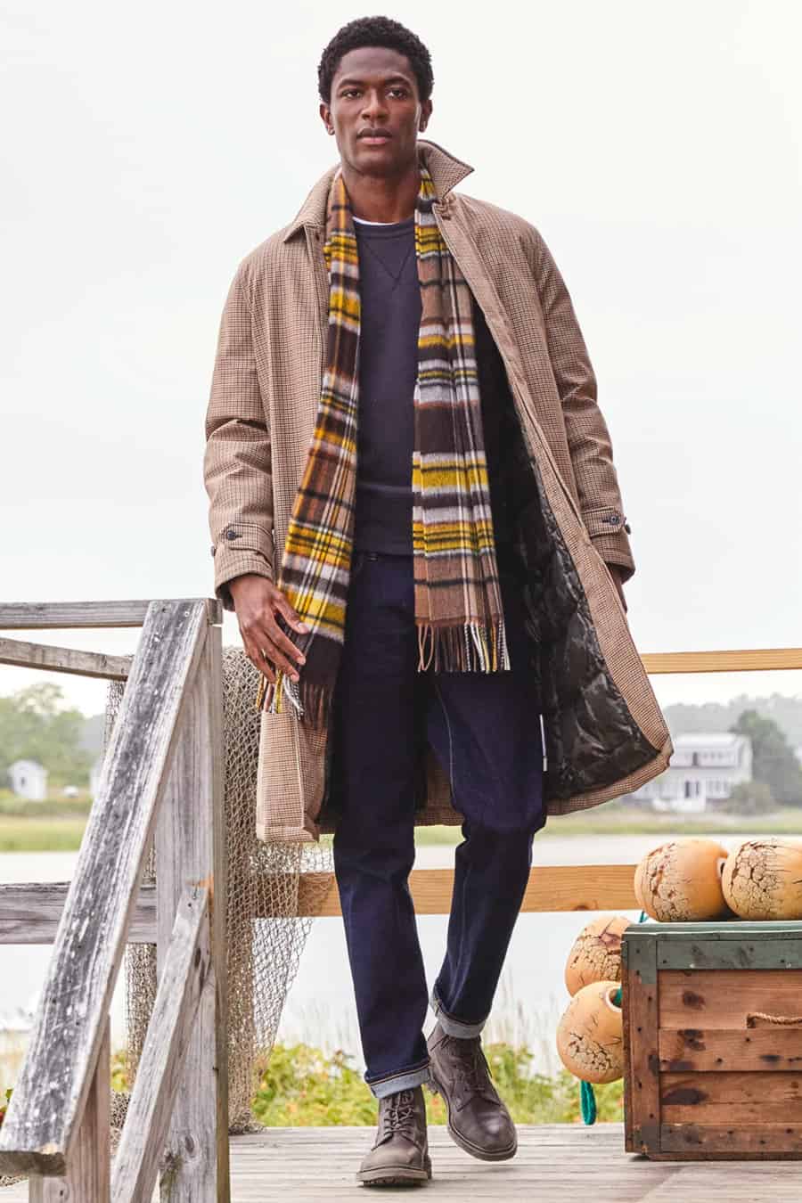Men's raw denim jeans, navy sweatshirt, beige rain coat, brown boots and yellow checked scarf outfit