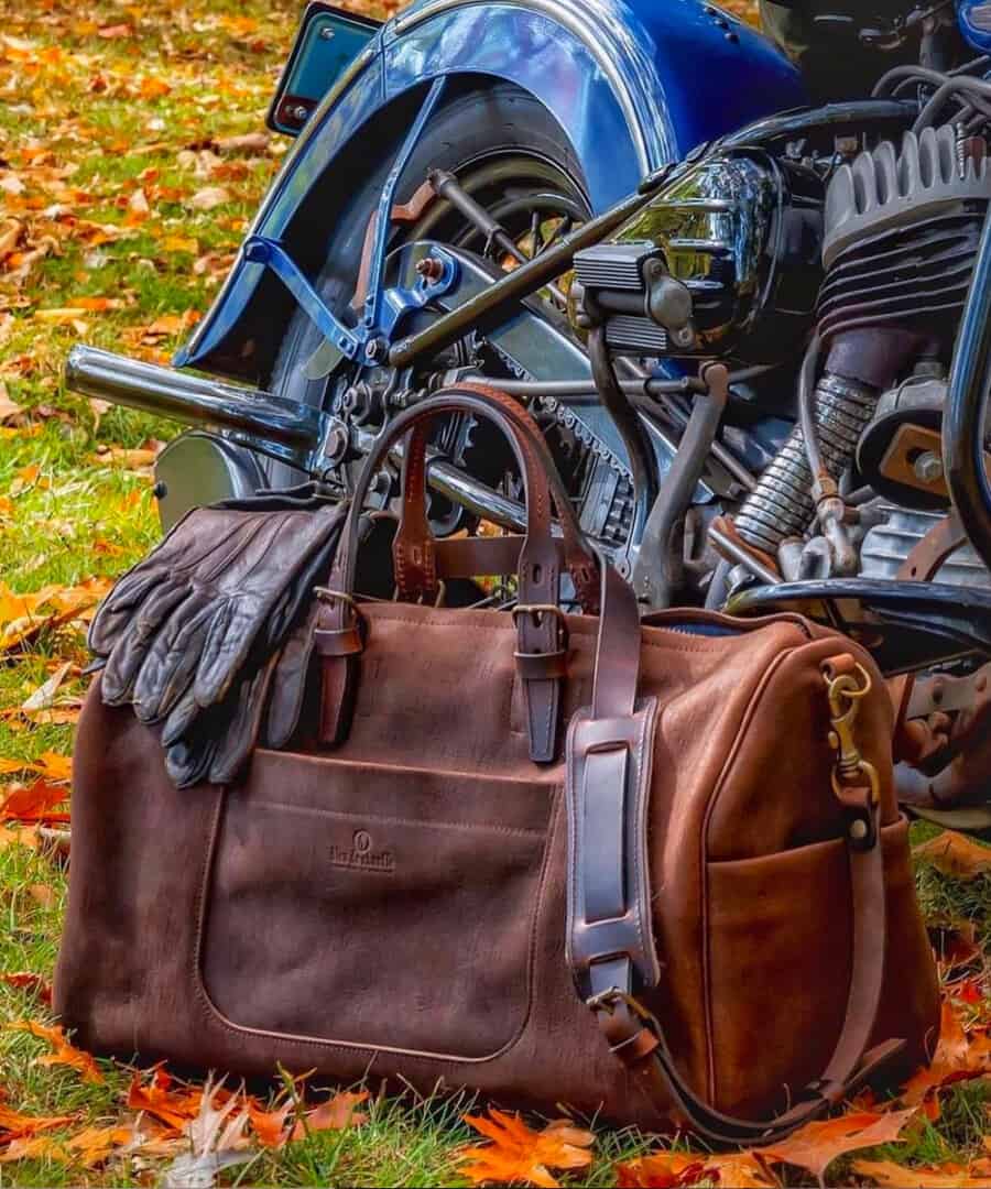 Weather leather weekender bag on grass in front of a motorbike