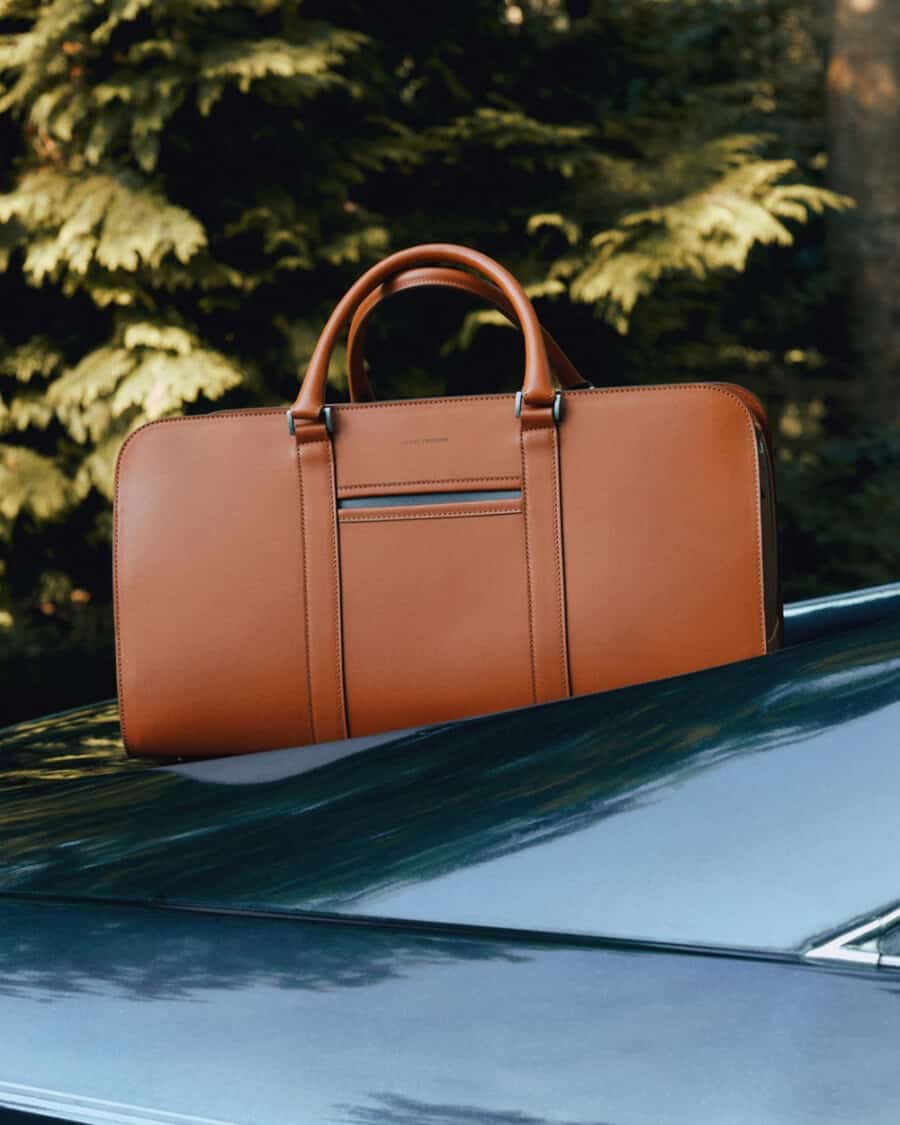A brown tan leather weekender bag by Carl Friedrik on top of a car