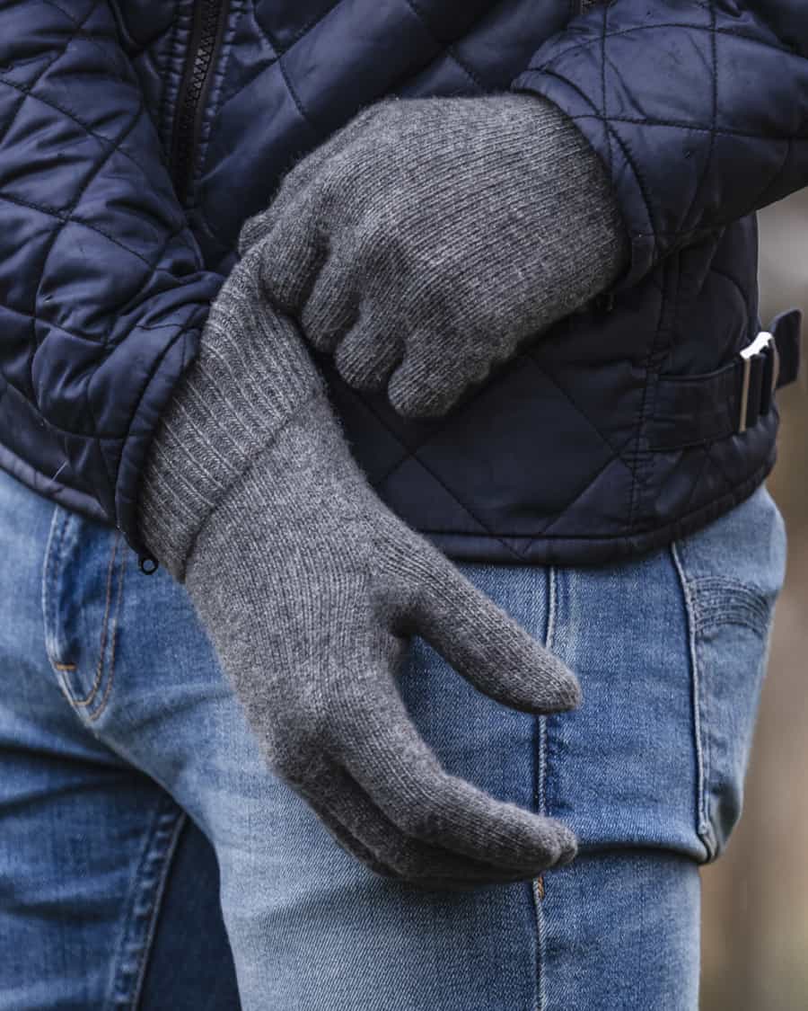 Man wearing grey knitted gloves, mid-wash jeans and a blue quilted jacket