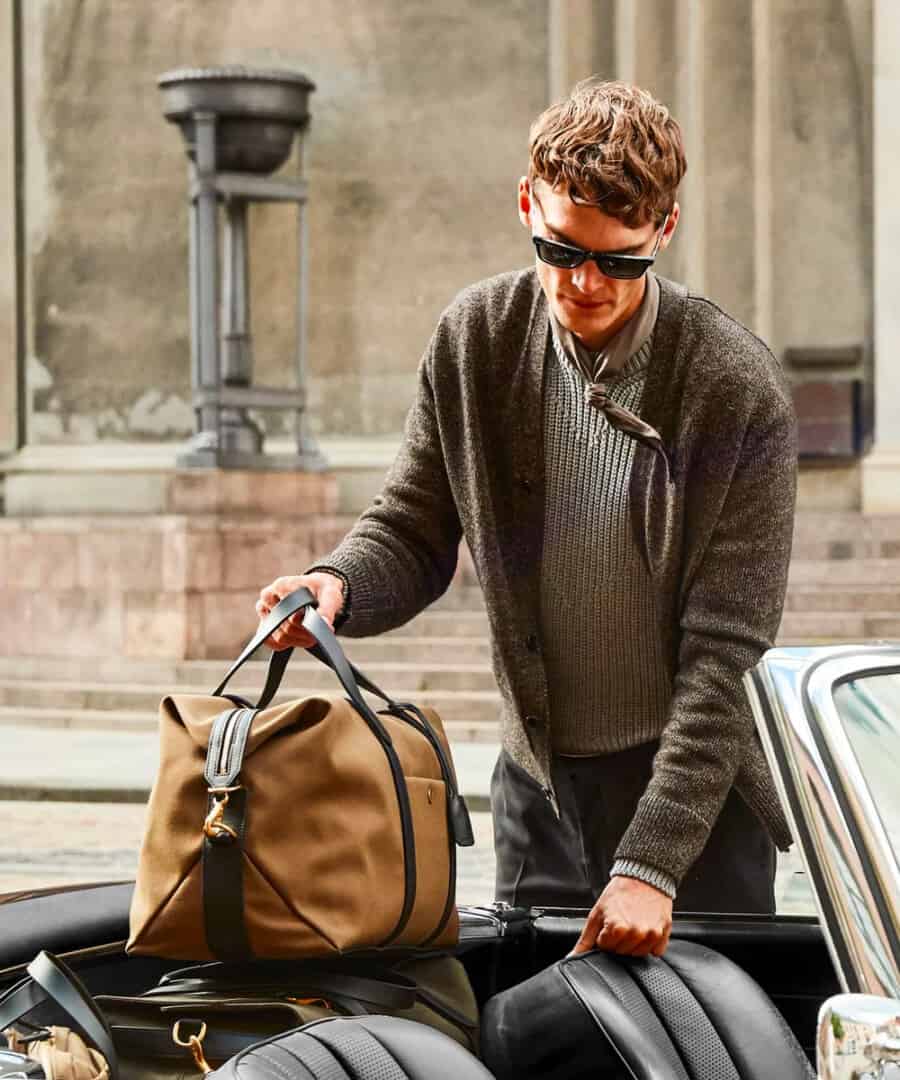Man putting a canvas weekender bag into the back seat of his convertible car