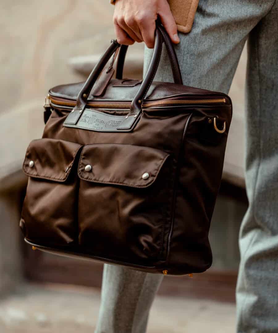 Man carrying a brown nylon weekender bag wearing grey trousers